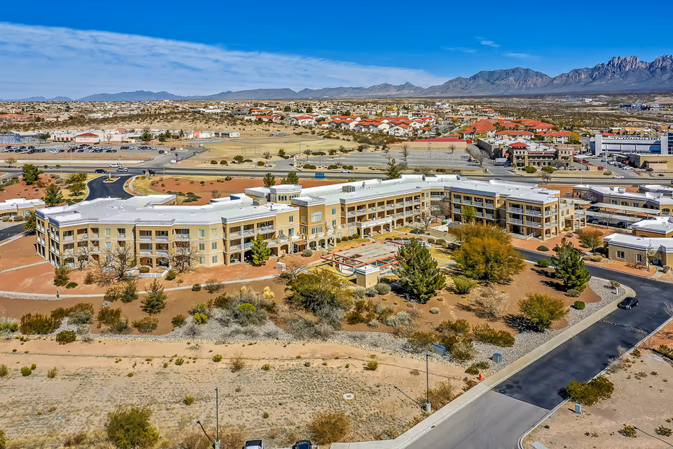 Aerial view of a three-story senior living complex set in desert landscaping with surrounding roads, parking, and distant mountains.