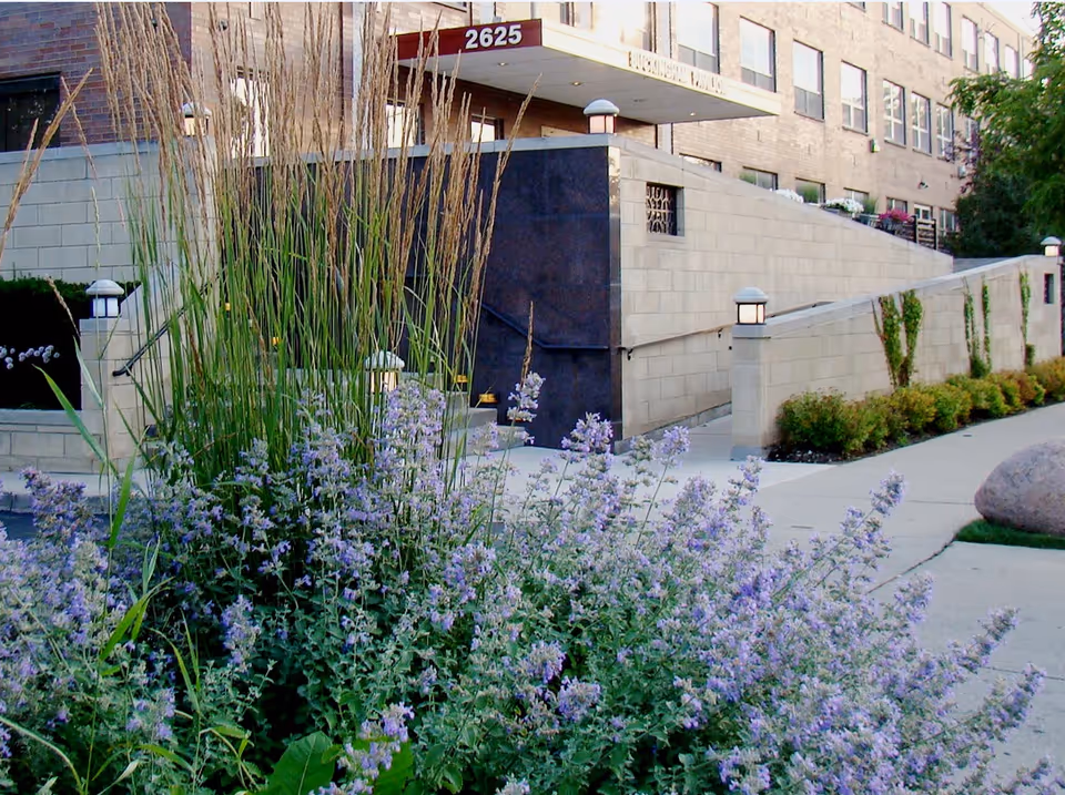 Front entrance of a nursing facility with purple flowering landscaping, a ramp, and a canopy marked 2625.