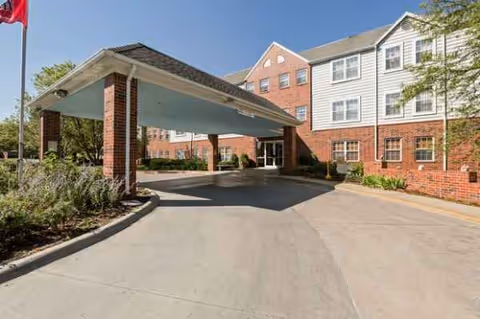 Exterior of a brick senior living building with a covered driveway and landscaped surroundings.