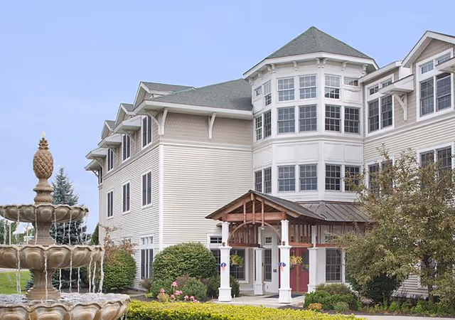 Senior living facility with a beige multi-story exterior, white trim, and a front fountain.