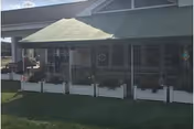 Covered front porch of a building with a green awning, white planter boxes and grass in the foreground.
