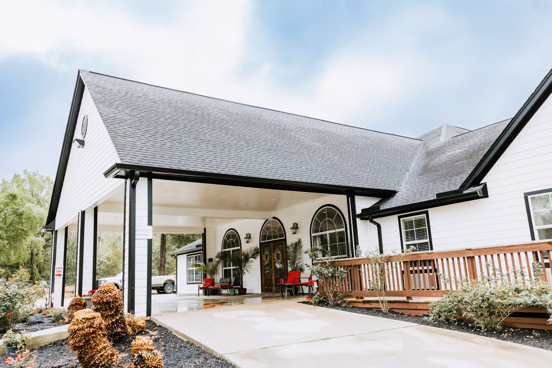 White senior living building with a covered entry and red chairs on the porch.