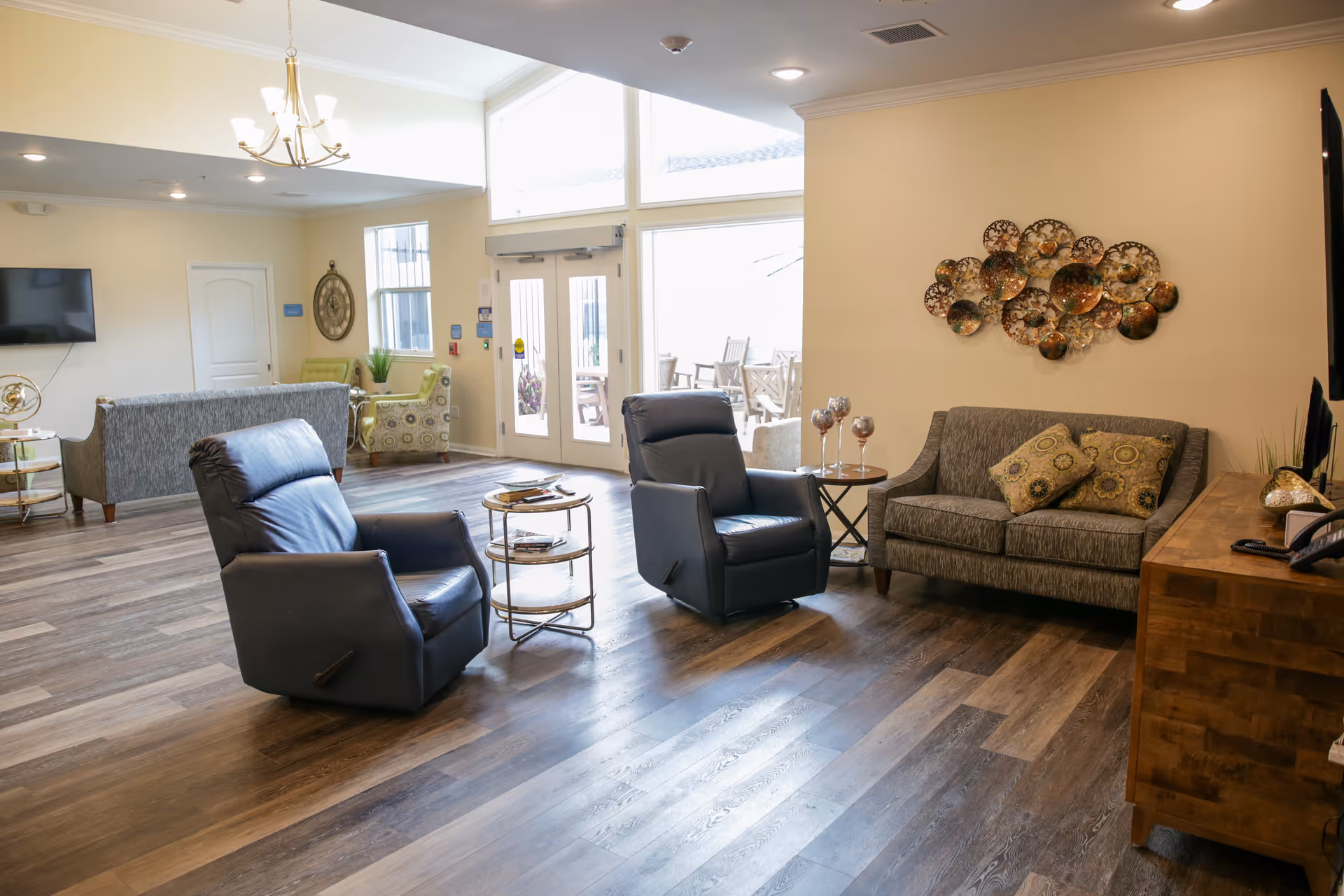 Bright common living room with two leather recliners, a sofa, side tables, and decorative wall art.