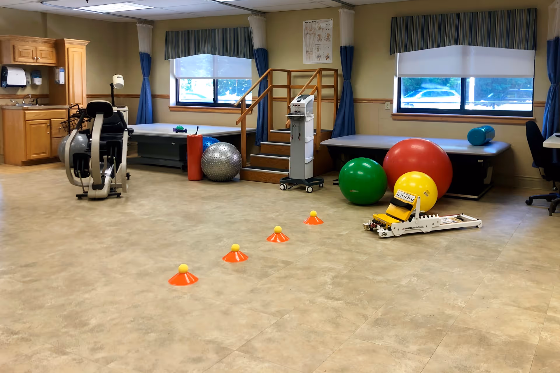 A spacious interior therapy room with exercise balls, cones, treatment tables, and rehabilitation equipment.