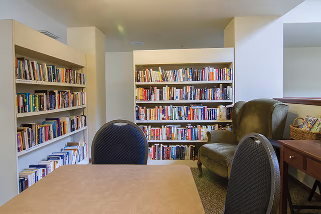Small library/reading area with bookshelves, a green armchair, and a table with chairs.