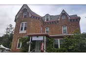 A brick historic-style building with a front porch and surrounding trees.