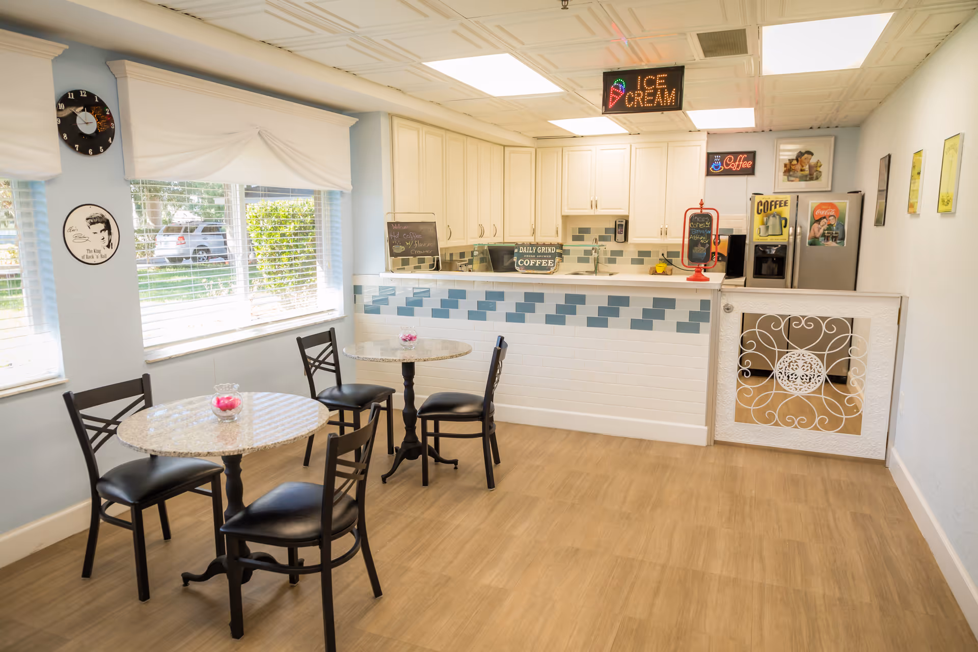 Bright small dining area with round tables and chairs facing a tiled service counter and coffee station.