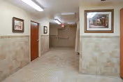 Interior hallway with tiled half-walls, framed artwork, several wooden doors, and an exit door at the far end.