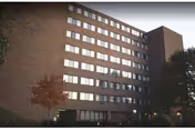Tall brick Webster Towers senior living building with many windows and surrounding trees.
