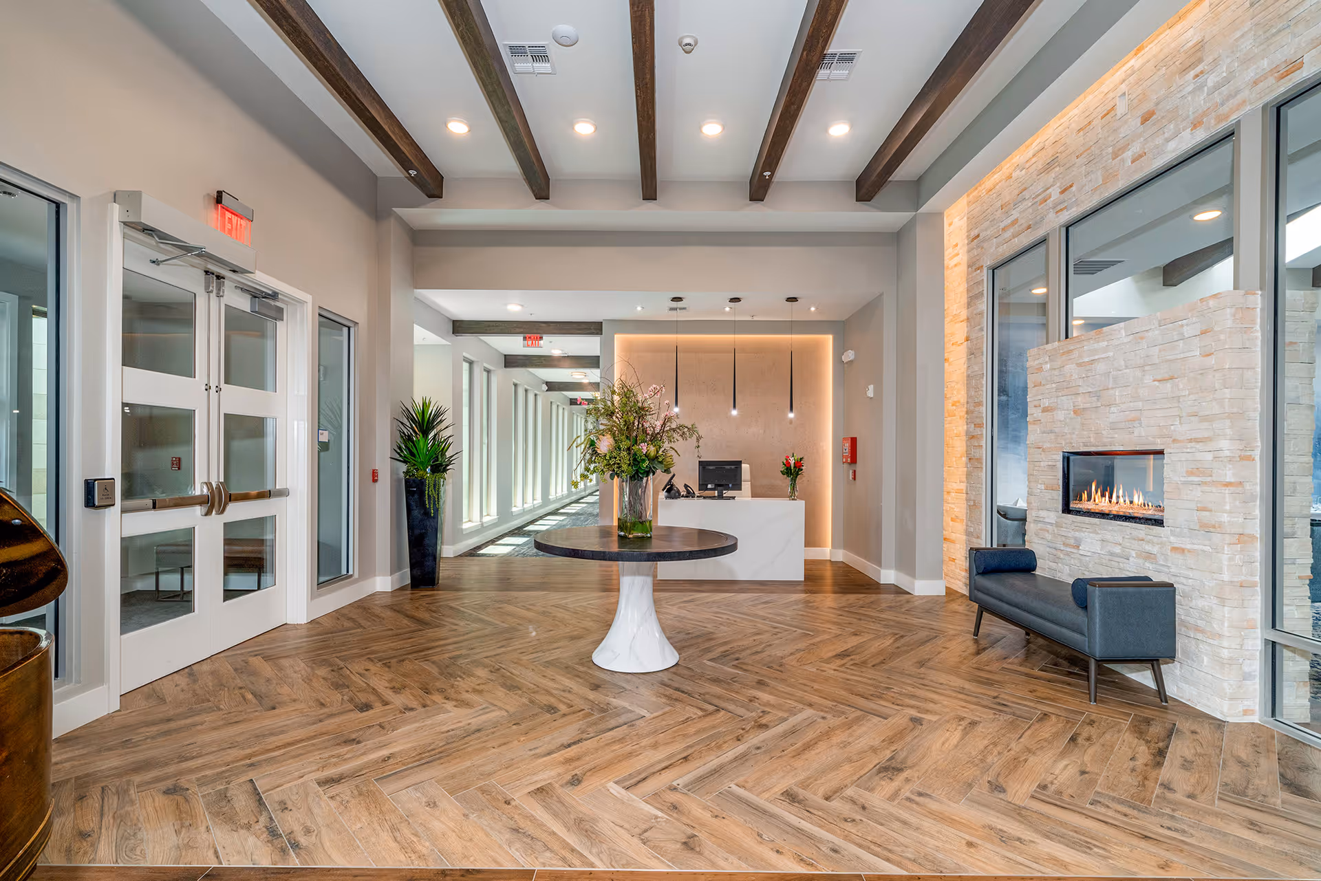 Bright modern reception lobby with a central round table, front desk, fireplace and seating.