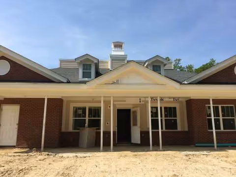 Brick facility exterior with a covered entrance and peaked roof, under construction.