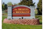 Outdoor sign for The Bridges at Brookline, a senior living community, mounted on a stone base with grass and trees in the background.