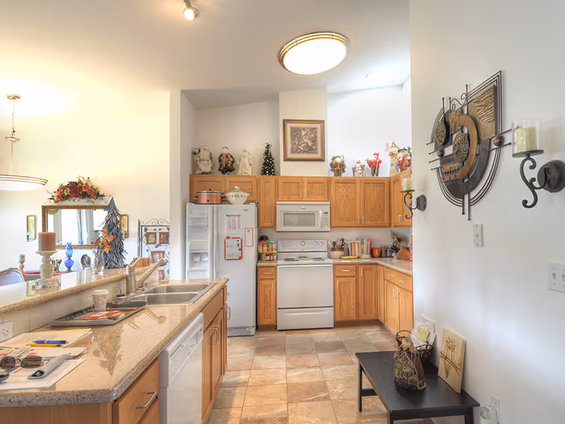 Bright kitchen with wooden cabinets, white appliances, a center island with sink, and decorative items on countertops and shelves.