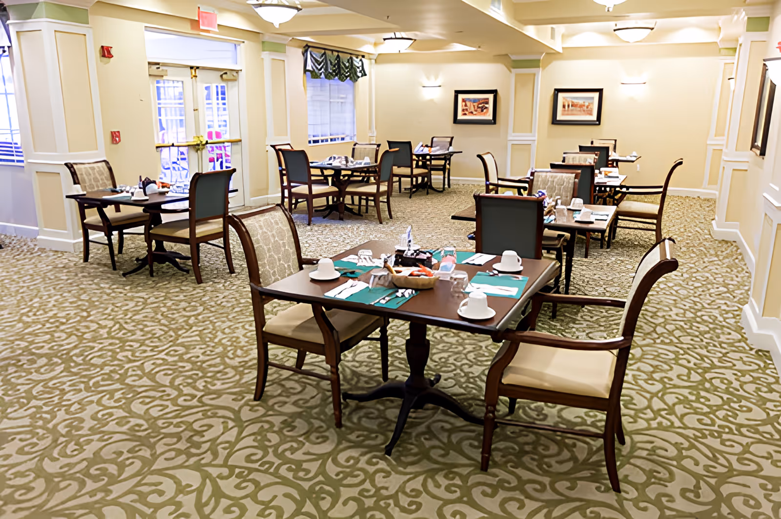 Bright, carpeted dining room with several set tables and chairs arranged for residents.