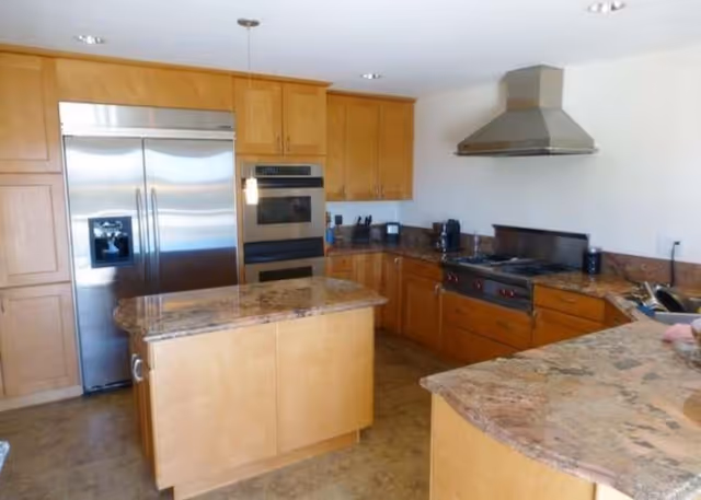 Open kitchen with stainless steel appliances, wooden cabinets, granite countertops, and a central island.