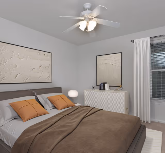 A neatly staged bedroom with a bed dressed in brown bedding and orange pillows, a ceiling fan overhead, a dresser with decor, framed wall art, and a curtained window.