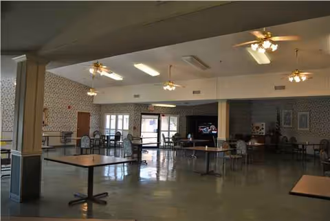 Interior dining hall with multiple tables and chairs in a senior facility.