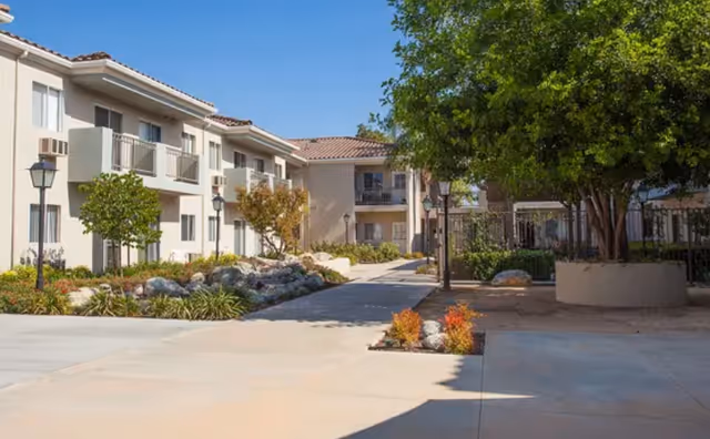 Sunny exterior view of Walnut Valley Senior Living with beige buildings and courtyards.