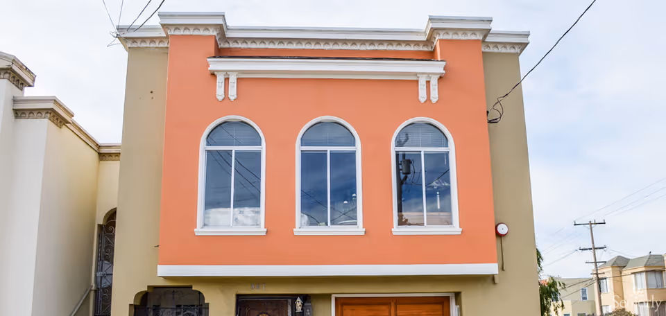 Front facade of a two-story peach-colored residential building with three arched windows above a garage.