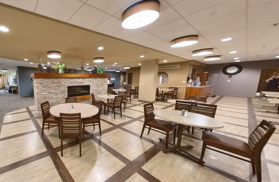 Spacious dining/lounge area with round and rectangular tables and chairs, a stone fireplace divider, and circular ceiling lights.