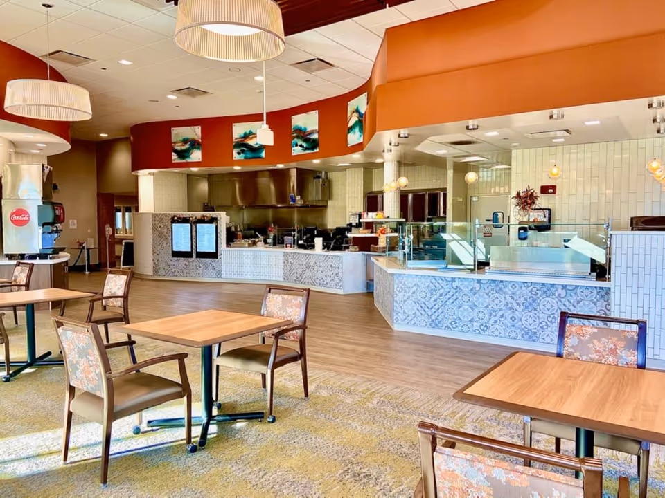 Spacious dining area with tables and chairs facing a serving counter and open kitchen.