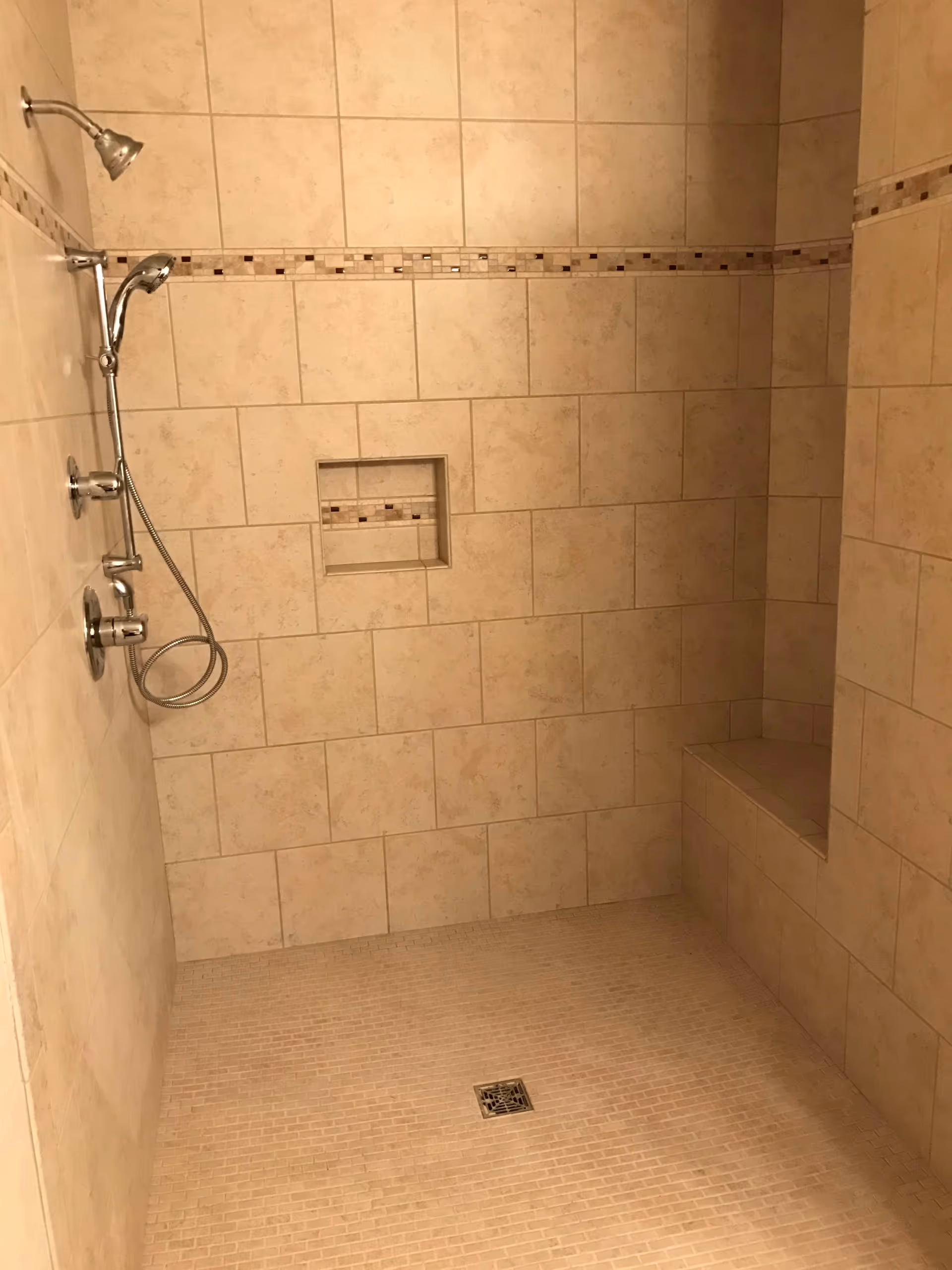 Tiled walk-in shower with a built-in bench, recessed shelf, and handheld showerhead.