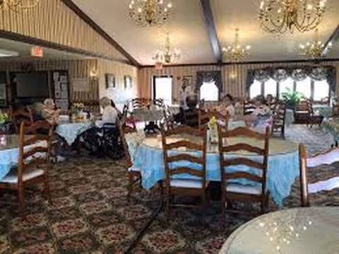 Senior living dining room with round tables, blue tablecloths, chandeliers, and residents dining.