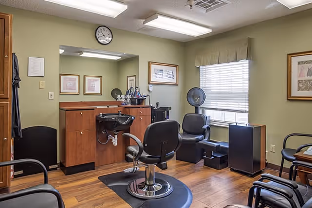 Interior salon room with styling chair, shampoo sink, hair dryer chairs, large mirror and window.