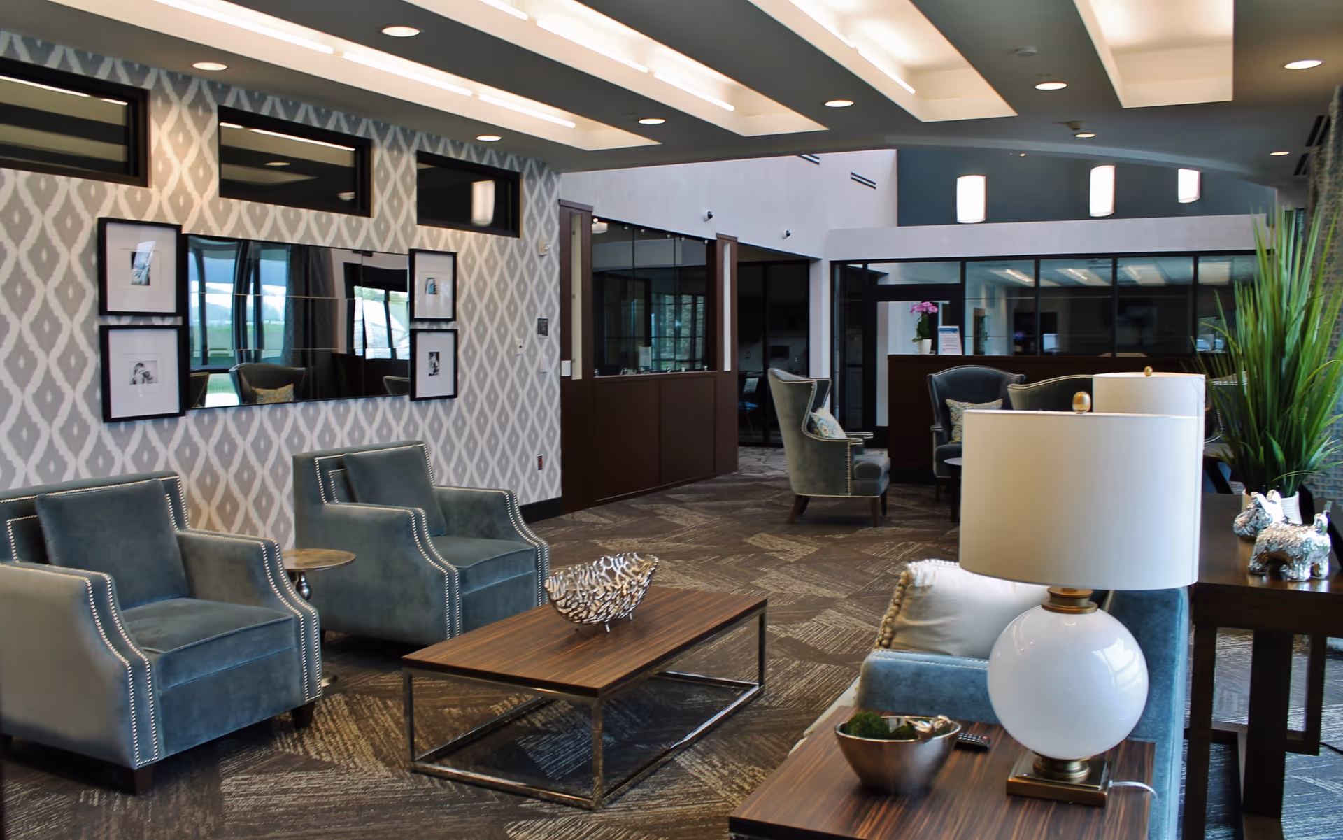 Spacious modern lounge with upholstered armchairs, coffee tables, lamps, and decorative wall art in a senior living facility.