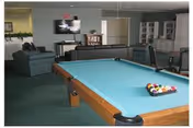 Community lounge with a pool table in the foreground, seating, a TV and bookshelves in the background.