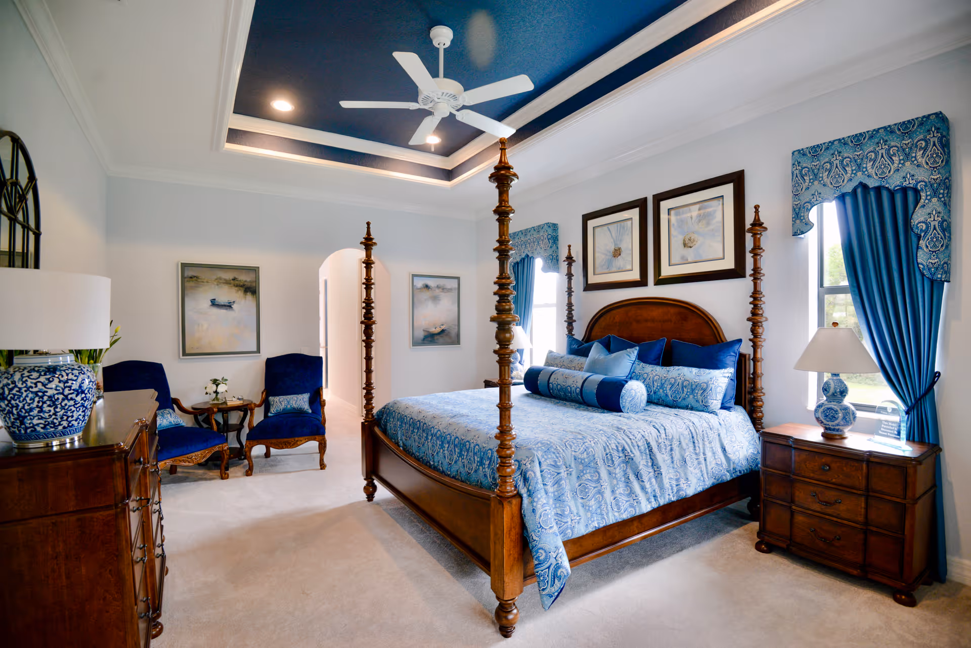 Elegantly furnished bedroom with a four-poster wooden bed dressed in blue patterned linens, matching drapes, bedside tables, and a seating area.