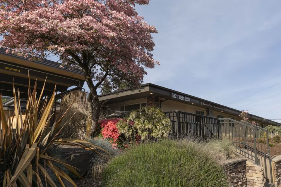 Exterior view of a single-story senior living center with a landscaped entrance and flowering trees.