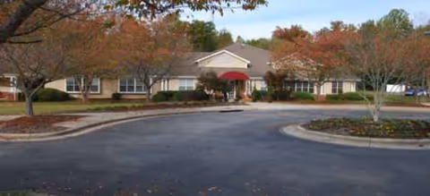 Senior living facility building front with driveway, trees, and a red entrance awning.
