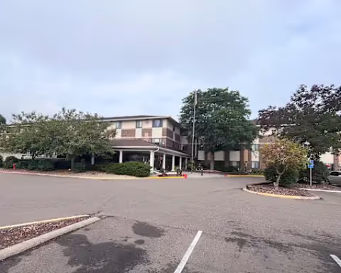 Front exterior of Oak Ridge Manor senior living facility with a driveway, parking lot, and surrounding trees.