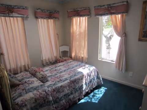 Small bedroom with a floral bedspread, multiple curtained windows, and green carpet.