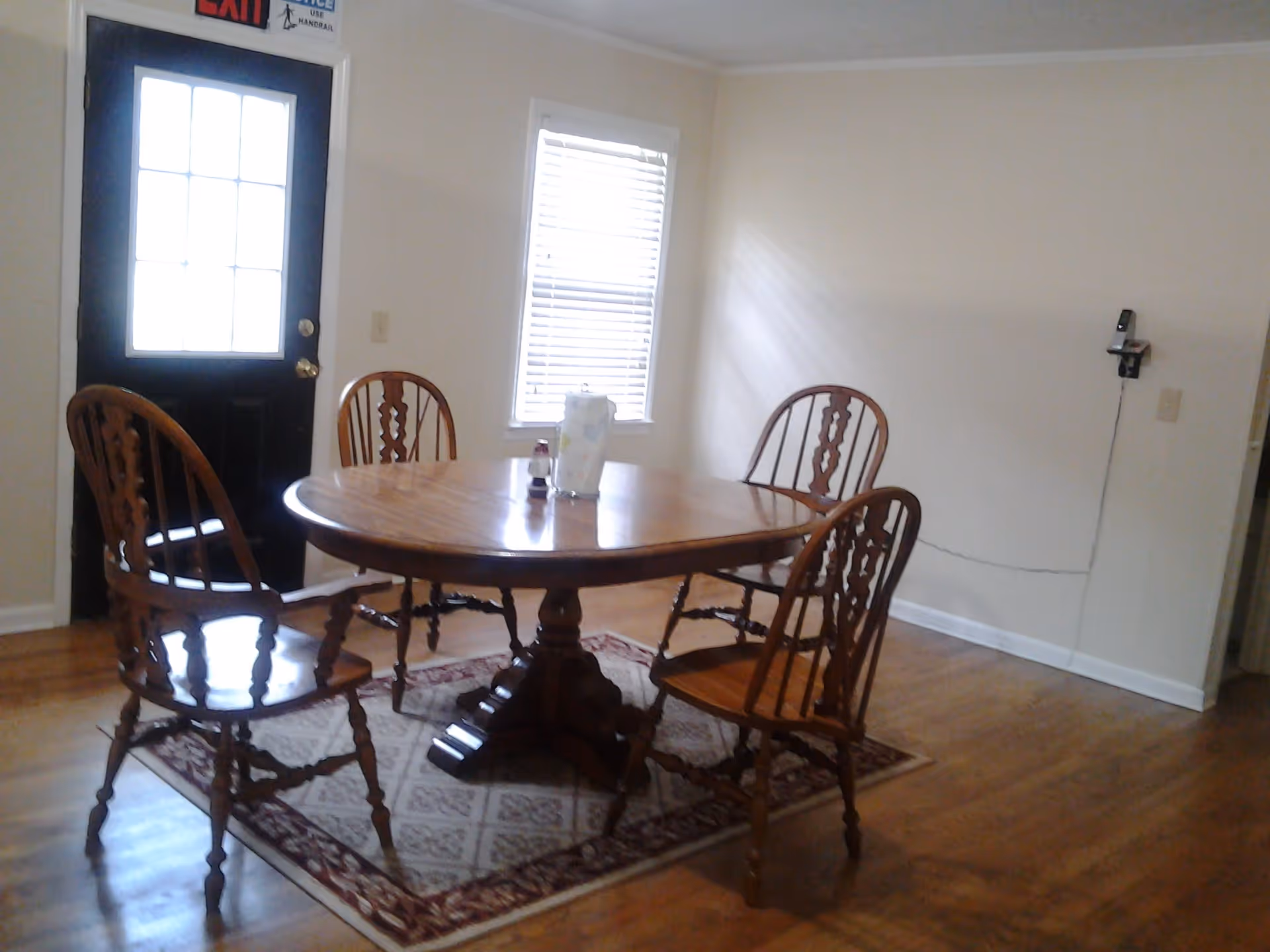 Small dining room with a round wooden table and four matching chairs on a rug near a door and window.