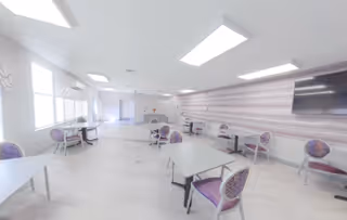 A bright, spacious common area with tables and chairs in a senior living facility.