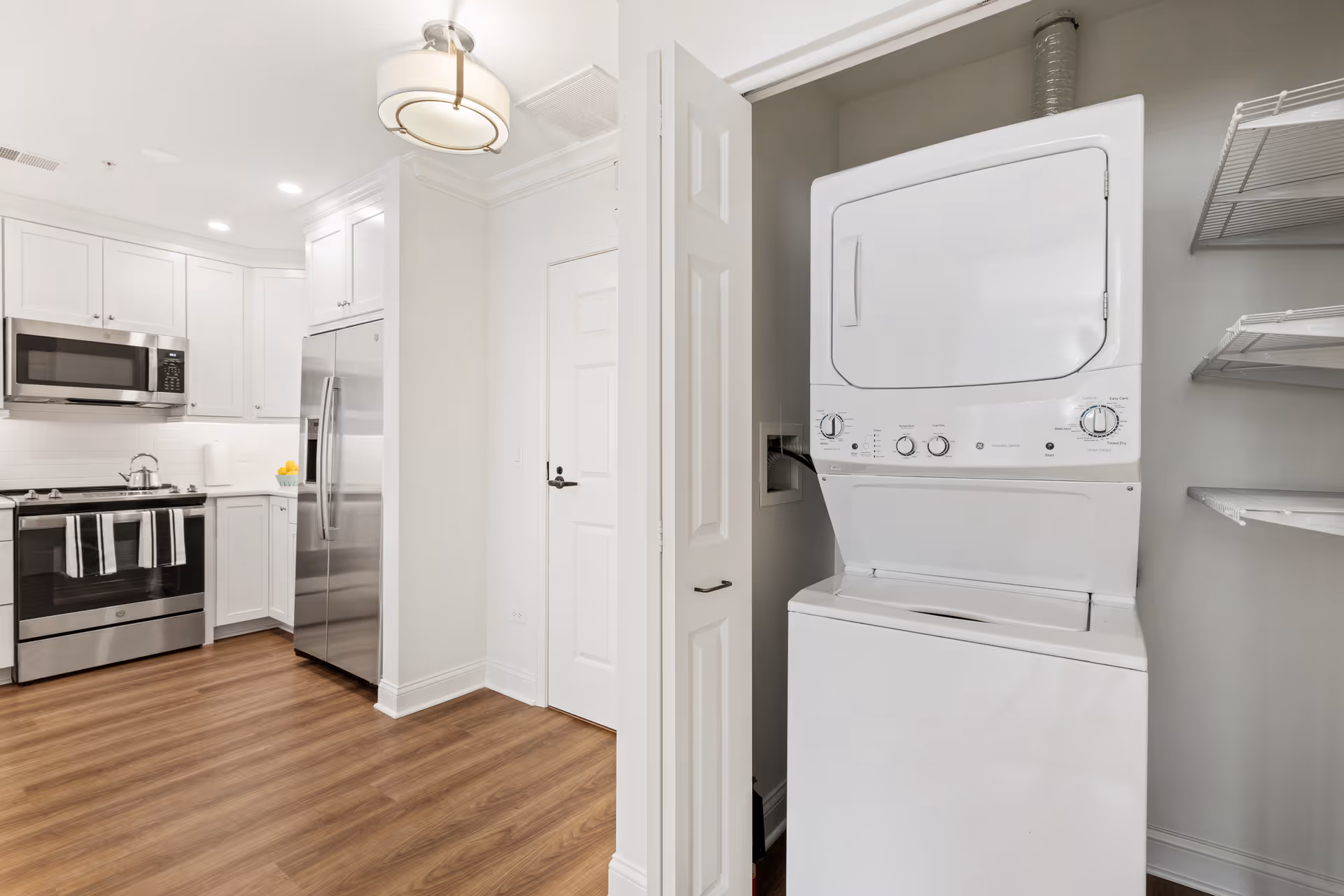 Modern kitchen with stainless steel appliances and an open closet revealing a stacked washer and dryer.