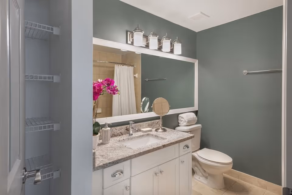 Modern bathroom with a granite-top vanity, large mirror, toilet, and a shower-tub with a white curtain.