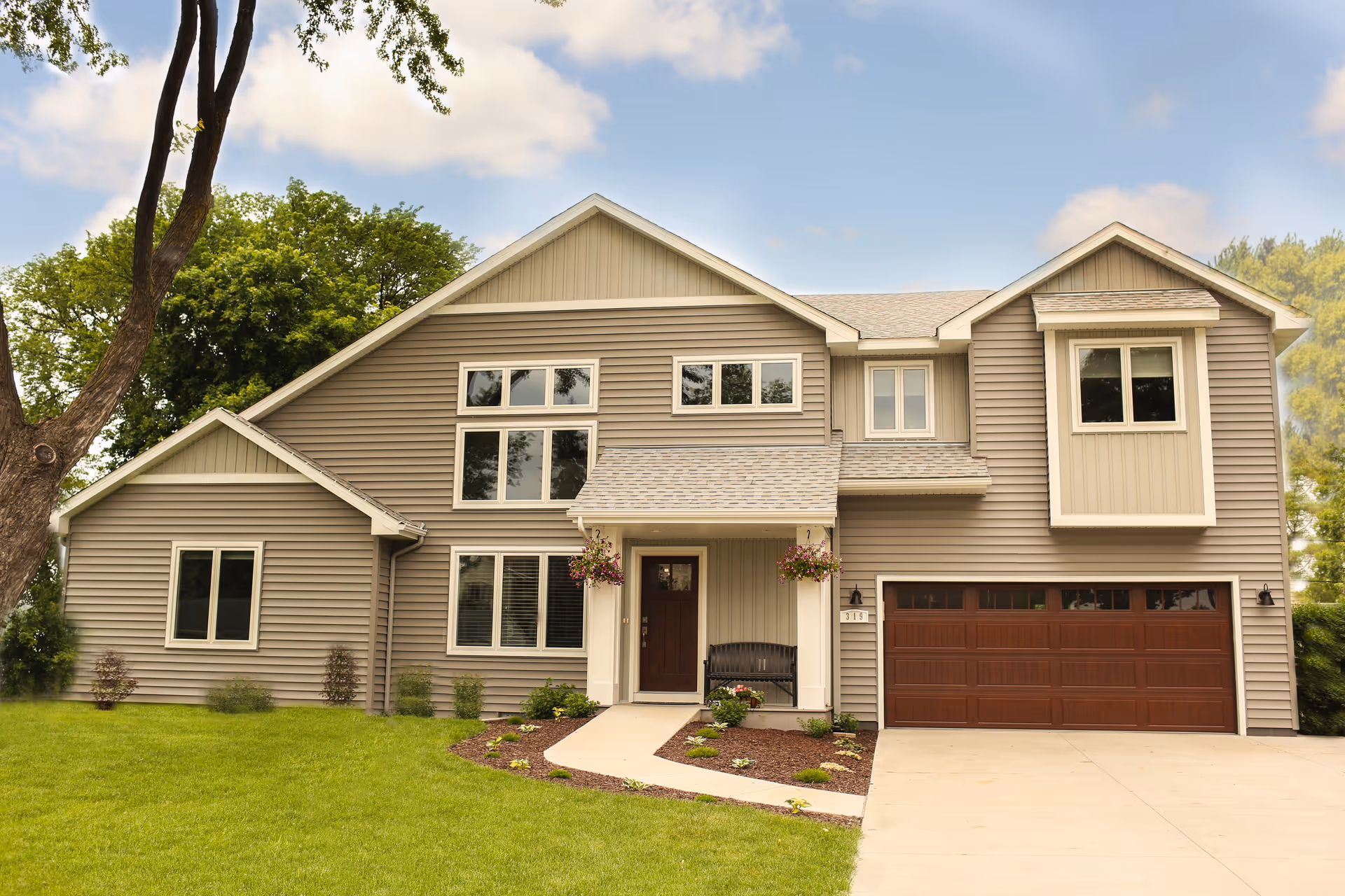 Two-story suburban house exterior with beige siding, a double garage, front porch, and a manicured lawn.