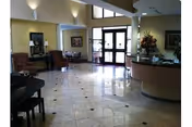 Entrance lobby with glossy tiled floor, a reception desk on the right, seating area on the left, and glass double doors ahead.