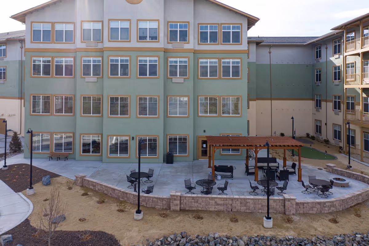 Outdoor courtyard with patio tables, chairs, a pergola and a multi-story apartment building facade.