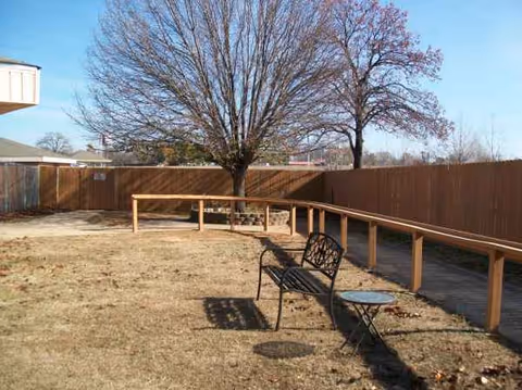 An outdoor courtyard with a bench, table, ramp, and a tree beside a wooden fence.
