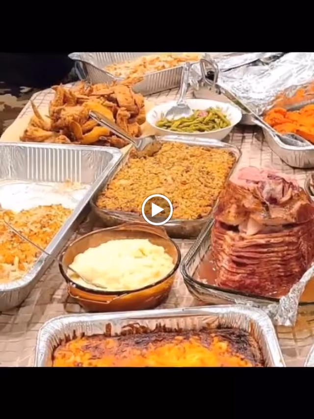 A buffet-style spread of various cooked dishes including sliced ham, mashed potatoes, green beans, fried chicken, and casseroles in aluminum trays and glass bowls on a table.