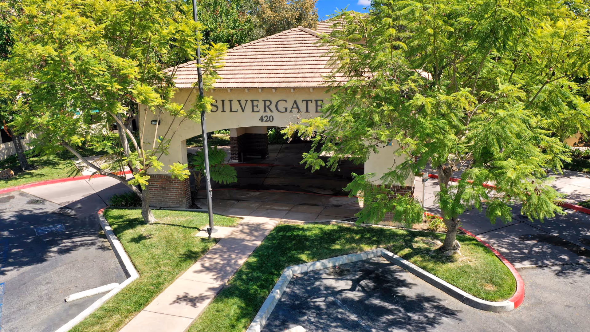 Entrance to Silvergate Fallbrook Retirement facility with a covered driveway, surrounded by green trees and landscaped grass areas.