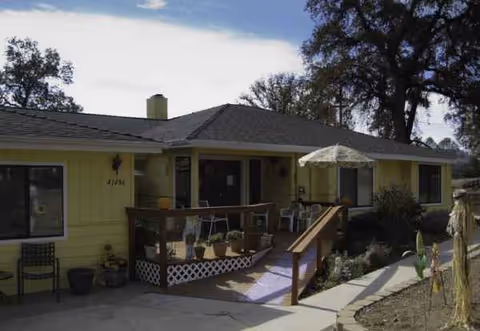 Front exterior of a single-story yellow facility with a ramp, porch, and outdoor seating.