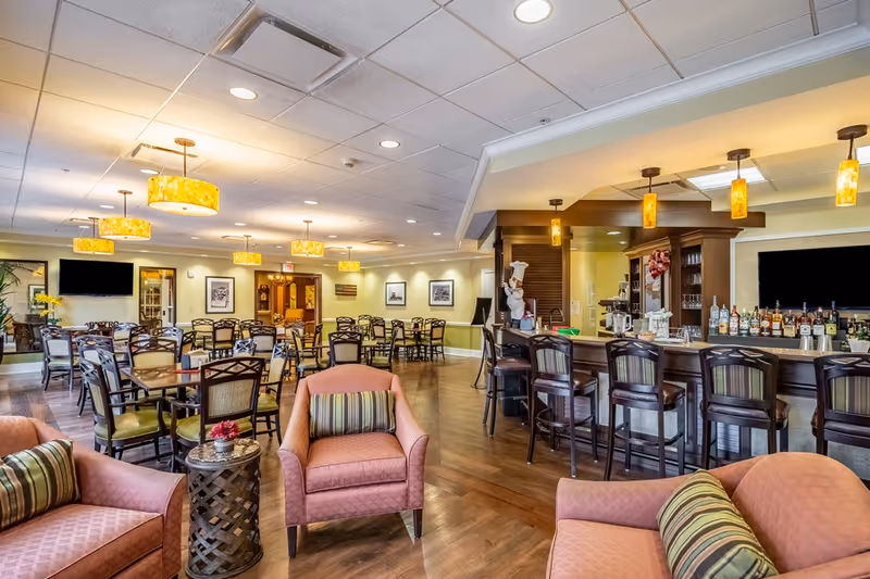 Spacious communal dining and lounge area with multiple tables and chairs, a bar with stools, and comfortable armchairs.