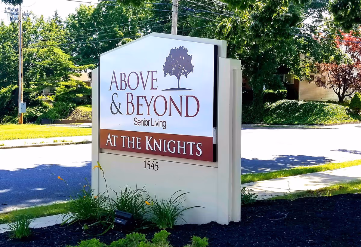 Freestanding roadside sign reading 'Above & Beyond Senior Living — At the Knights' with address 1545 in a landscaped front area.