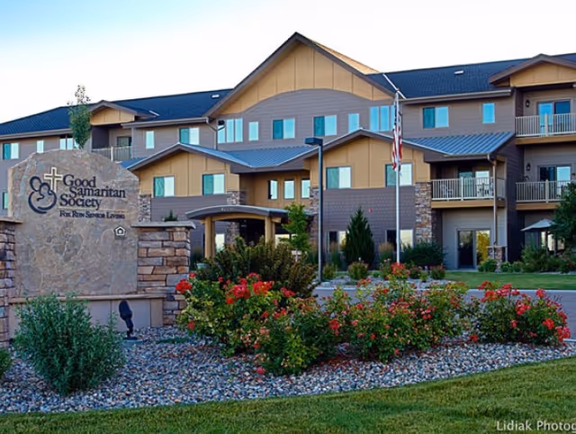 Front exterior of the Good Samaritan Society - Fox Run Senior Living building with landscaped entrance, sign, and an American flag.