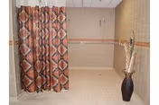 Tiled walk-in shower area with a patterned shower curtain, dual showerheads, and a decorative floor vase.